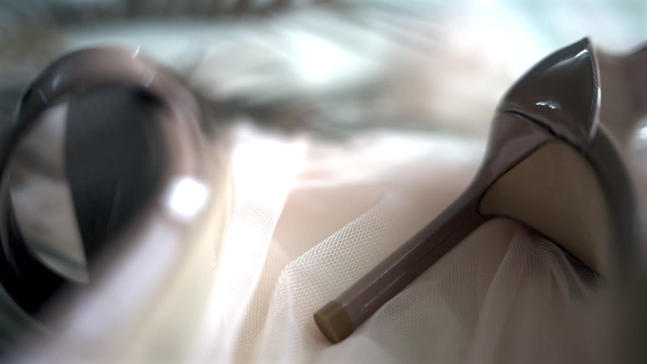 A beige pair of strappy heels near a bag on a piece of tulle