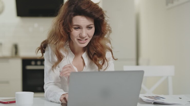 Lächelnde Frau liest erfreuliche Nachrichten am Laptop.