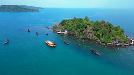 tourist boats surrounding a small tropical island in koh rong, cambodia, with crystal clear water and lush vegetation. dramatic aerial view flight wide orbit overview drone