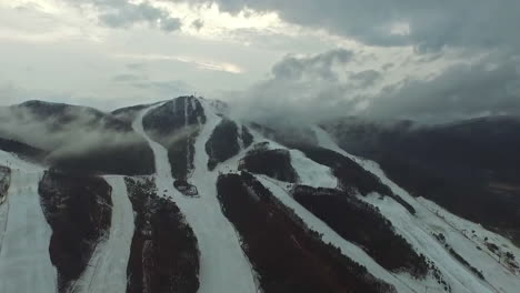 slow motion drone view slowly zooming in on partially snow covered mountains, overcast sky and fluffy clouds