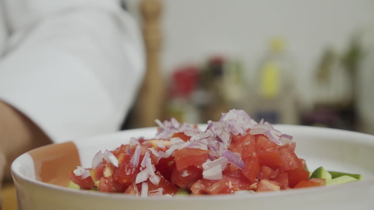 요리사는 칼날에서 잘게 썬 양파 조각을 야채 샐러드와 함께 접시에 밀어 넣습니다.