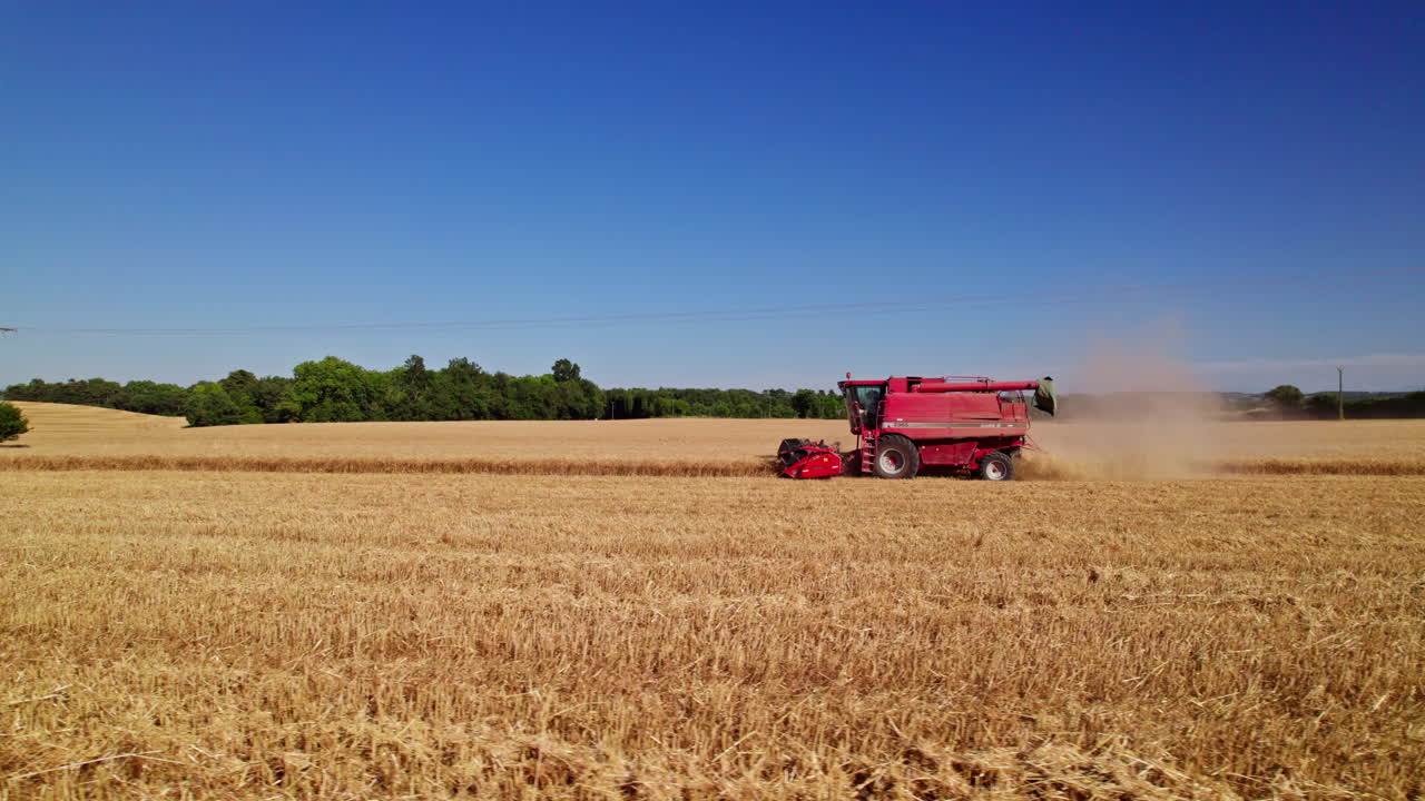 A wide, low aerial shot tracking a combine harvester from the side as it harvests wheat. from right to left. REC709, UHD, 23,976 fps