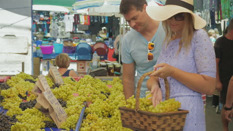 Pareja-Eligiendo-Uvas-Y-Hablando-Con-Una-Sonrisa-En-El-Mercado-Al-Aire-Libre-De-Tesalónica,-Grecia