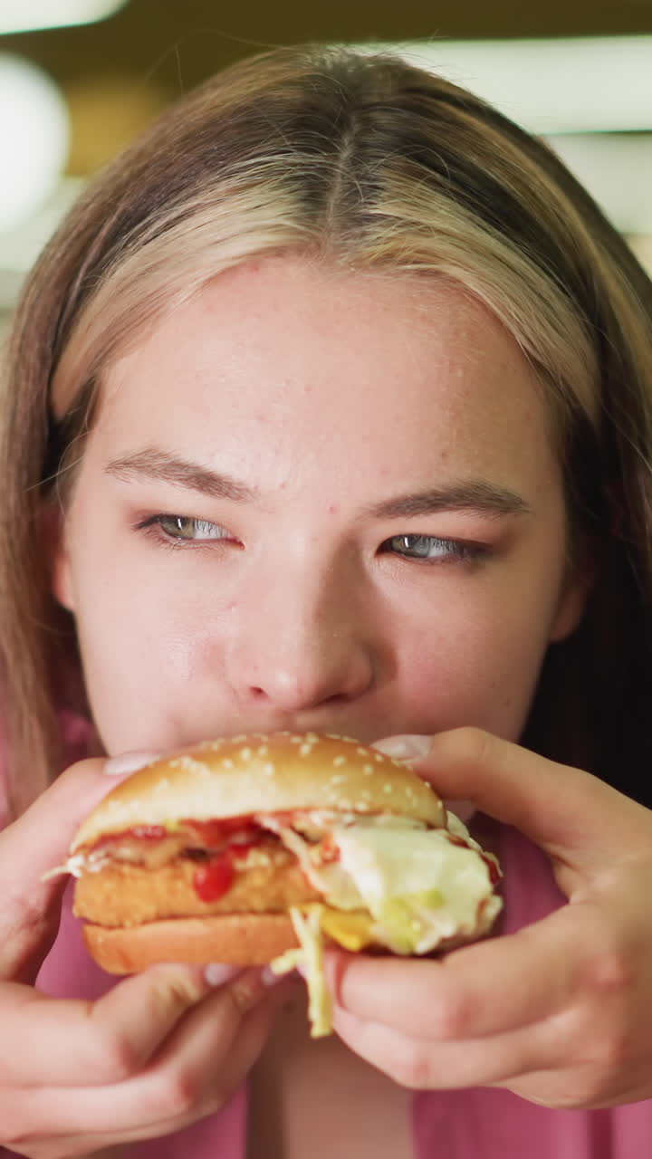 dama de vestido rosa toma un bocado de hamburguesa, masticando lentamente con los ojos bien abiertos, ella parece pensativa, saboreando la comida con enfoque, el fondo está suavemente borroso, con efectos de luz bokeh