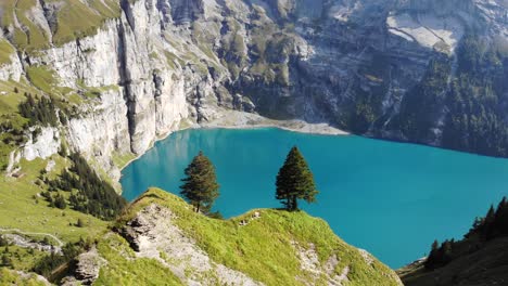 sobrevuelo aéreo sobre árboles con vistas al lago turquesa oeschinensee en kandersteg, suiza, rodeado de acantilados