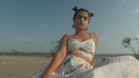 young-adult-lady-female-hipster-gen-z-teen-girl-serious-face-with-knot-hair-and-nose-piercing-wearing-earrings-looking-at-camera-posing-on-the-beach,-sunny-head-body-shot-portrait