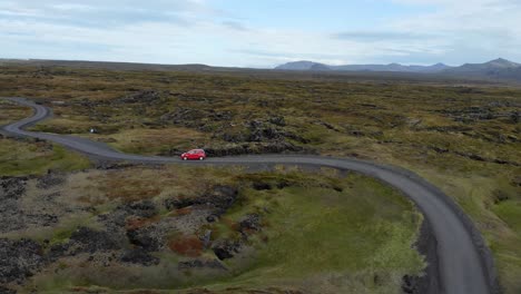 Antena-De-Un-Pequeño-Coche-Rojo-En-Una-Carretera-Con-Curvas-En-El-Paisaje-De-Islandia