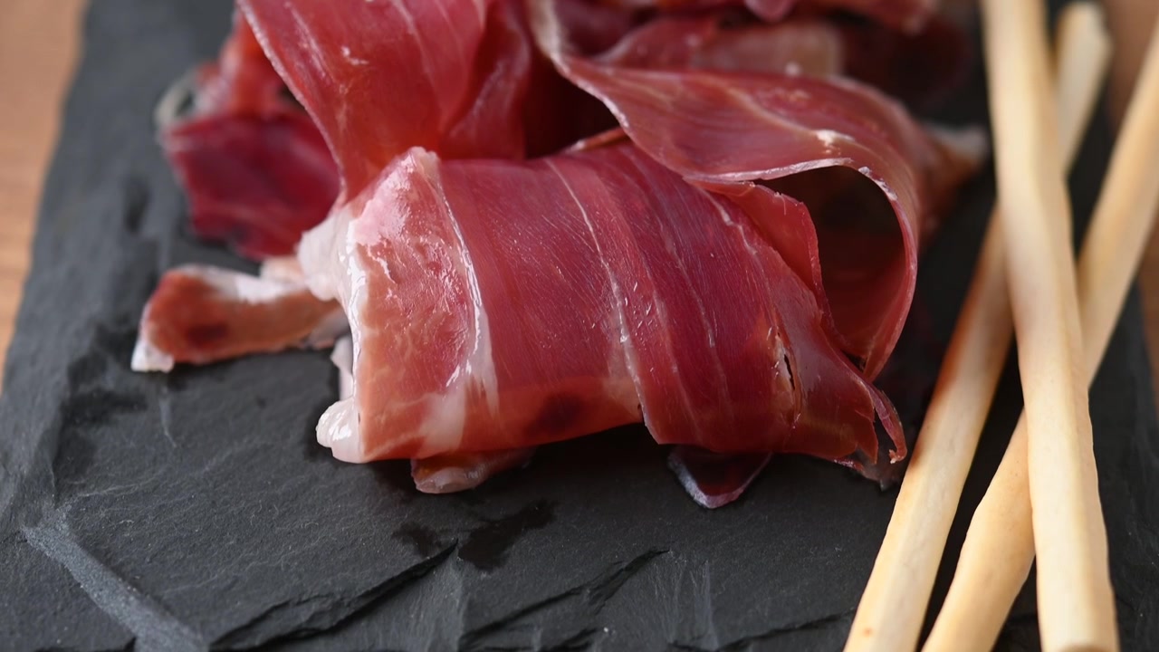 Fette di prosciutto stagionato servite su un tagliere di ardesia con grissini