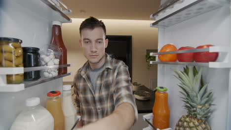 a young man takes a container with breakfast from the refrigerator. view from inside the refrigerator