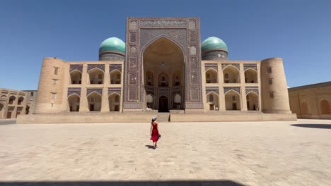 4K-Gimbal-Shot:-Young-Woman-Approaching-Mir-i-Arab-Madrasa,-a-UNESCO-Heritage-Site-in-Bukhara-Old-Town,-Uzbekistan