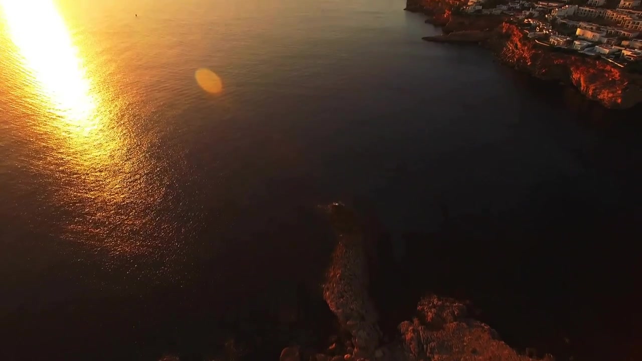 Drone subindo e fazendo panorâmica, mostrando um promontório iluminado pelo sol, enquanto pontos de falha piscam, destacando a costa