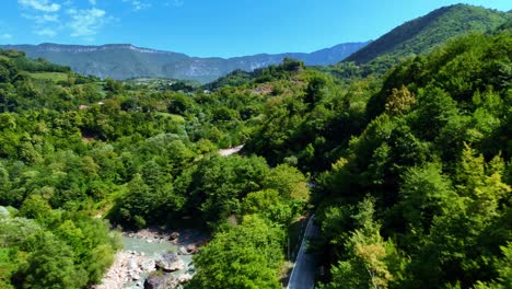 aerial drone view of fast-flowing river winding through lush green valley with broken bridge remains in faro, portugal. mountain background and vibrant forest create scenic natural landscape.