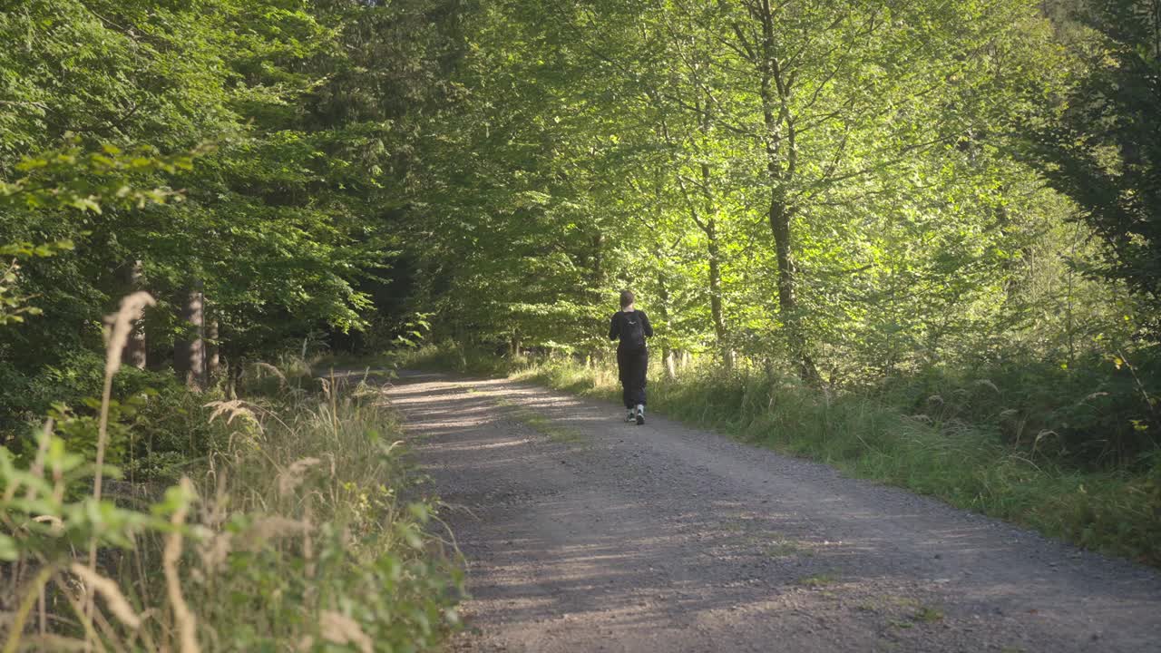 Young girl with a backpack goes to the forest in the golden sun. Escape to nature from the city, relax among the trees