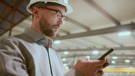 low angle of focused engineer using mobile phone in industrial plant