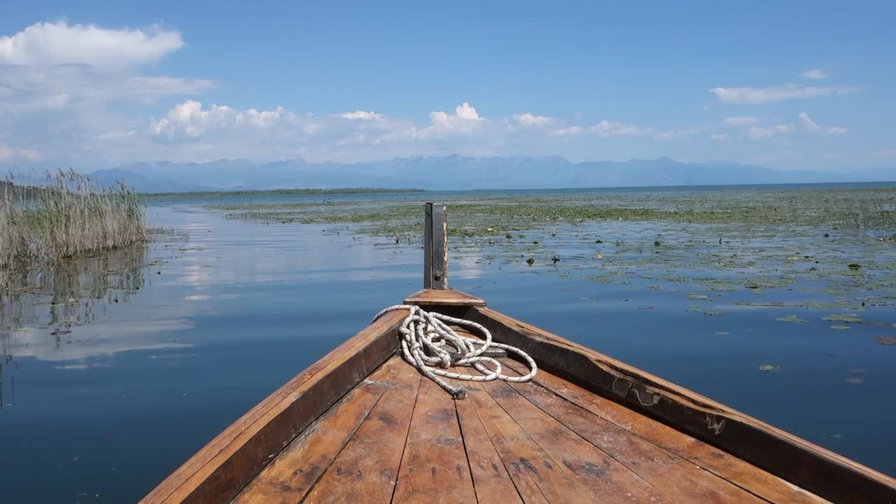 wooden boat sails calmly on waters of Lake Skadar on sunny day. Albania and Montenegro border. Largest lake in Southern Europe