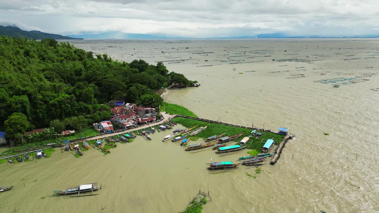 Wide aerial pass captures a riverside village with boats, aquatic plants, and vibrant homes nestled between water and dense greenery