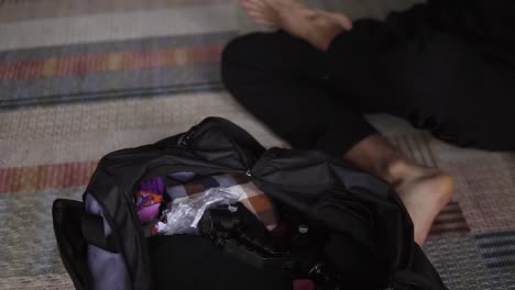 hombre irreconocible empacando bolsa negra con ropa para viajar en la sala de estar, de cerca