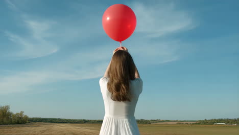woman releasing a red balloon into the sky