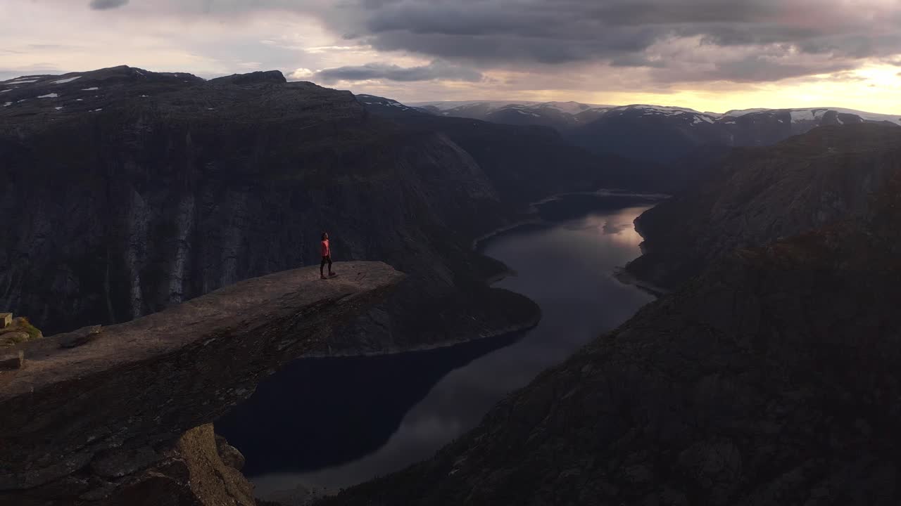 A woman stands on a cliff in Norway, enjoying the breathtaking view of the valley below, Trolltunga