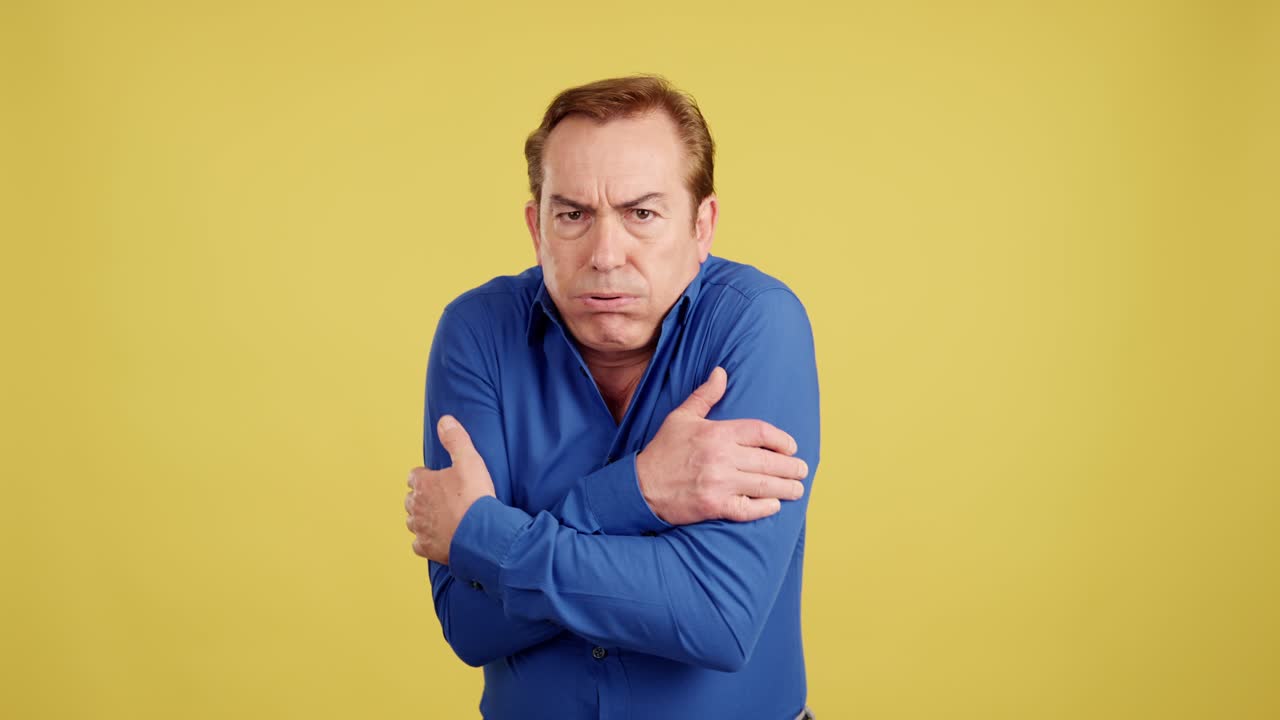 Man shivering and hugging himself due to cold on a yellow background