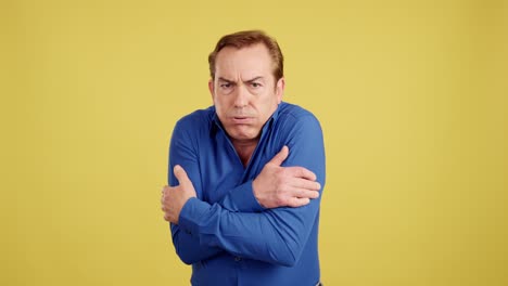 man shivering and hugging himself due to cold on a yellow background