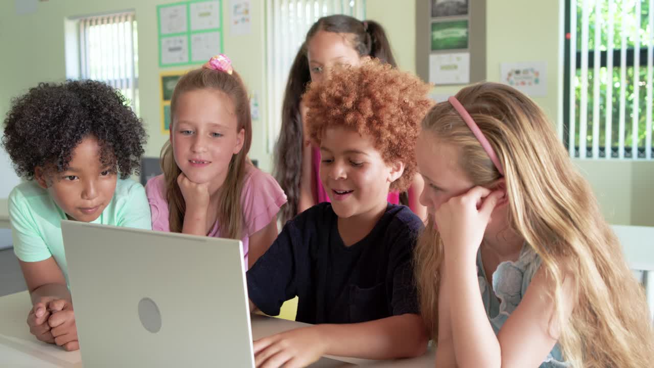Diverse kids at school crowding around laptop, watching, boy pressing keys, girl touching screen