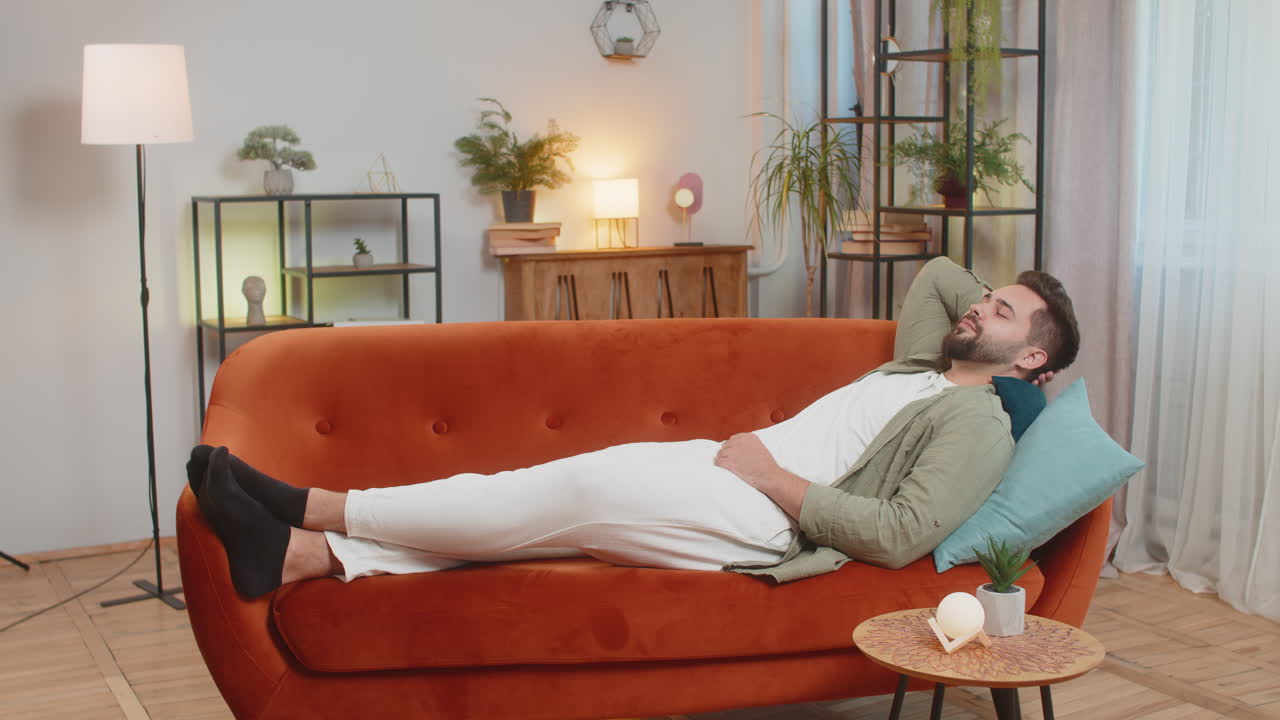 Tired caucasian handsome young man enjoy relaxing lying on sofa in living room at home apartment