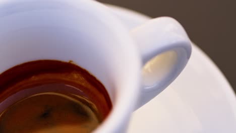 panning left to a super close-up, macro shot of a delicious espresso inside a café cup in italy, highlighting the smooth crema