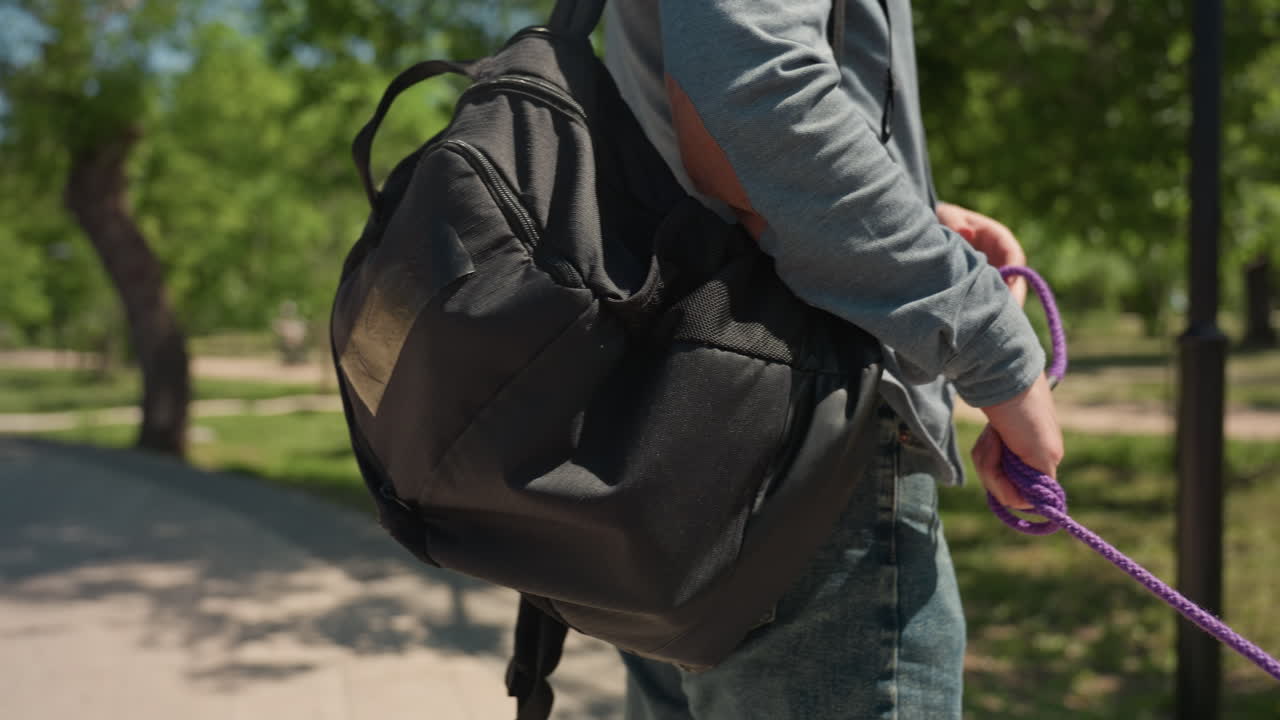 mano sujetando la correa, paseo urbano con correa y pack, vista cercana de una mano sujetando una correa morada mientras camina, toma detallada de una mano agarrando la correa durante una excursión urbana al aire libre con mochila