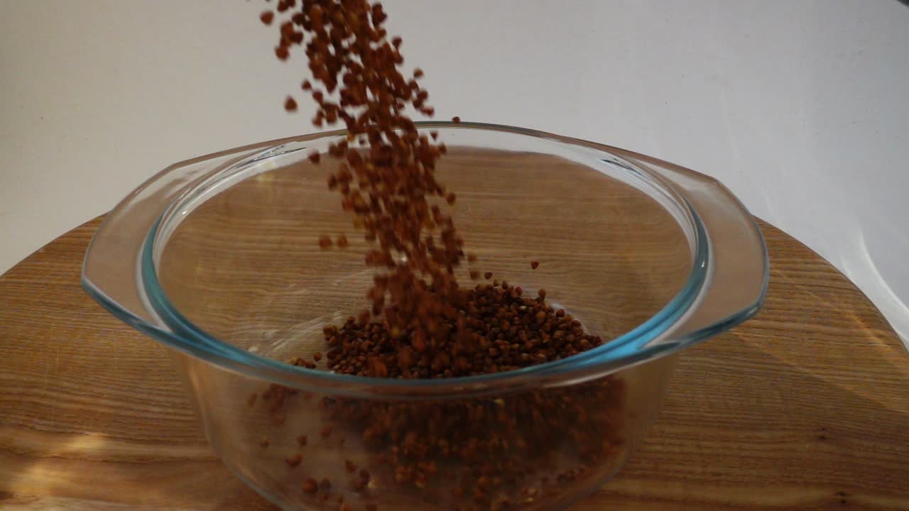 Filling of buckwheat boiled water in a glass pan. Slow motion