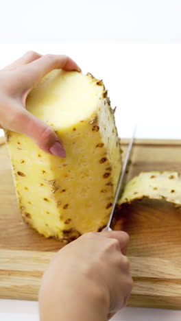 peeling pineapple on a cutting board. female's hands cleaning fresh exotic fruit with a knife. tropical food. vertical video