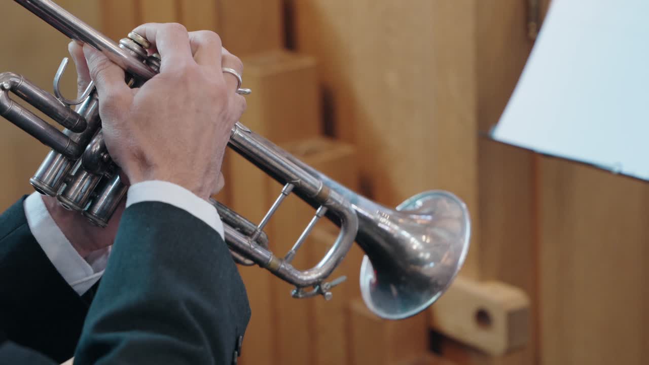 Primo piano di un trombettista che suona una tromba d'argento in un ambiente formale, con spartiti visibili sullo sfondo
