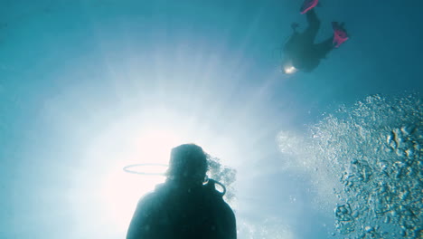 cinematic slow motion shot of scuba diver filmed from below with the sun from above and bubbles in the frame, 120fps, slomo