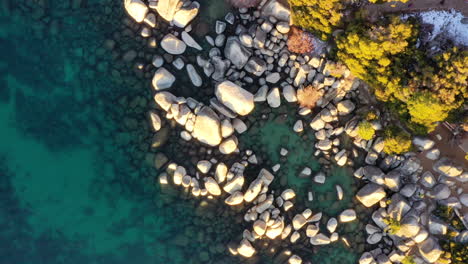 Rocky-coastline-of-crystal-clear-lake-during-winter-season,-top-down-descending-view