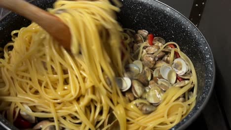 stirring delicious linguine pasta and clams with wooden forks in hot pan