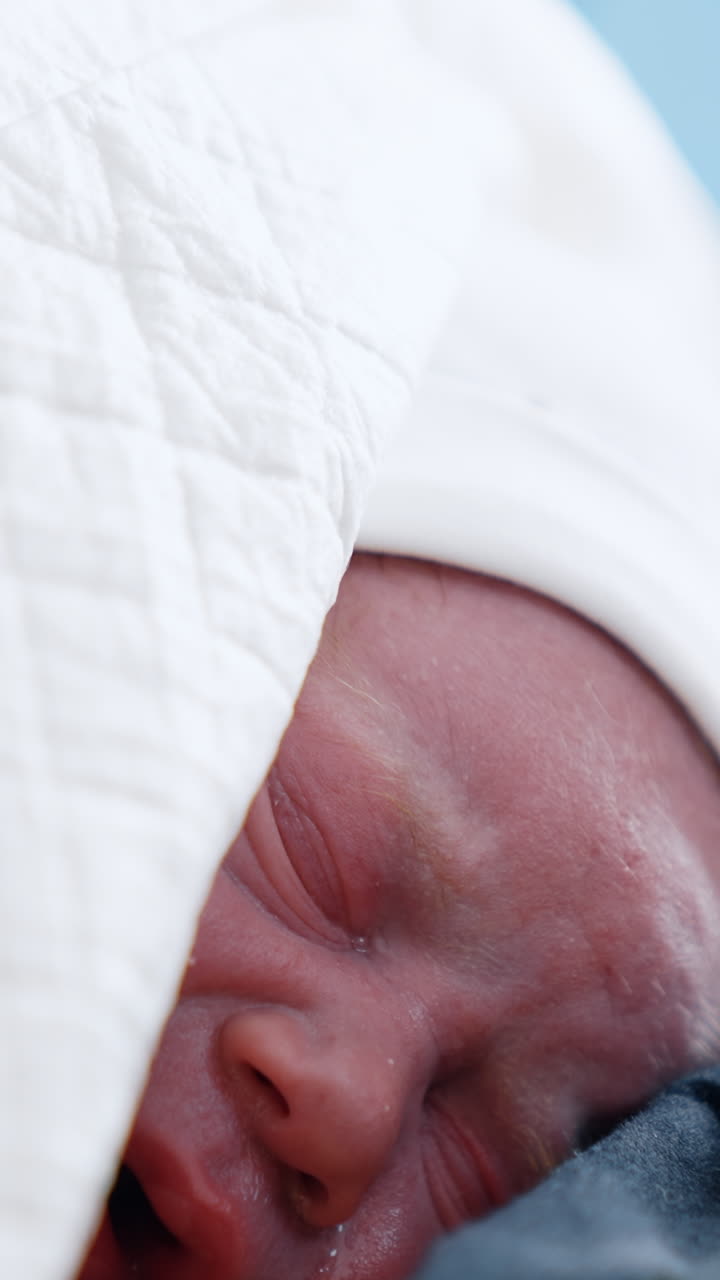 Neonato piccolo e rosso che piange sdraiato sul petto della mamma. Bambino appena nato coperto da coperte. Ritratto ravvicinato. Video verticale
