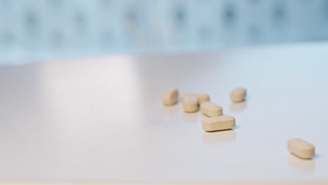 Vitamin-tablets-falling-down-on-white-surface-table-and-bouncing-around,-Shallow-depth-and-motion-blur