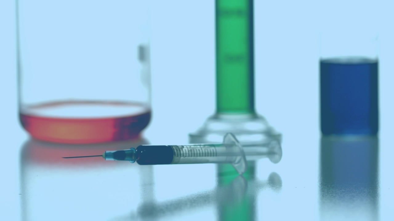 Animación de cuadrados rojos girando sobre una jeringa y vasos de laboratorio con reactivo sobre un fondo azul.