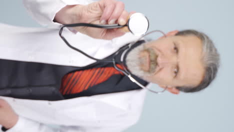 Vertical-video-of-Old-doctor-listening-to-camera-with-stethoscope.