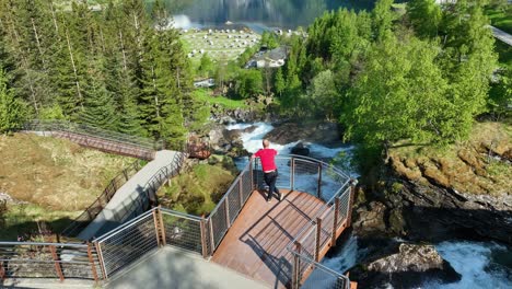 tourist on viewpoint beside geiranger river -forward moving aerial with slow tilt up revealing stunning geiranger fjord and mountain landscape