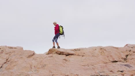 Senior-hiker-woman-with-backpack-and-trekking-poles-walking-on-the-rocks