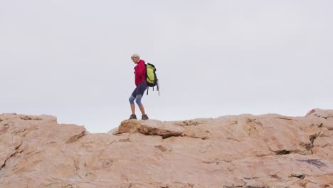 senior hiker woman with backpack and trekking poles walking on the rocks