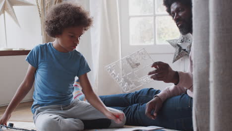 black middle aged father sitting on the floor at home helping his pre-teen son find the pieces of a toy construction kit, close up