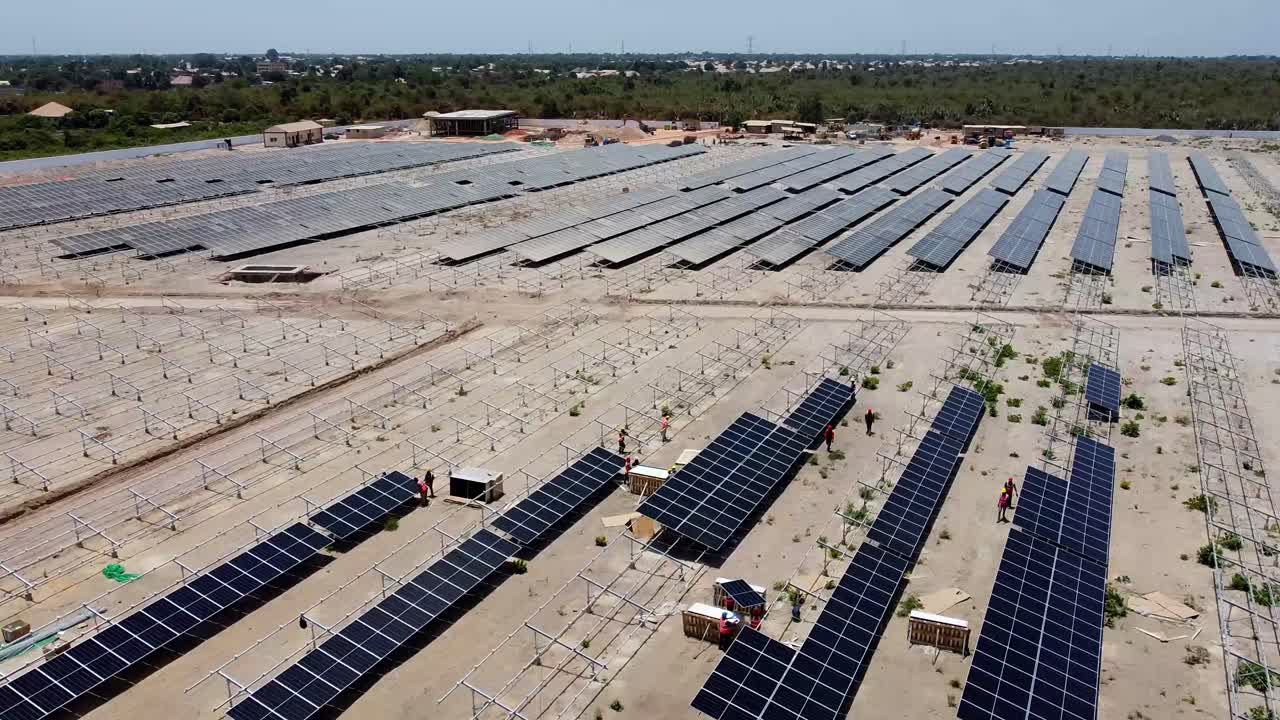 Aerial forward dolly view of technicians and engineers working installing bifacial solar panels at Jambur solar PV project site under construction in Gambia, West Africa