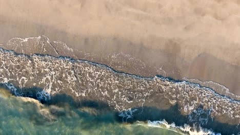 aerial view waves break on white sand beach.