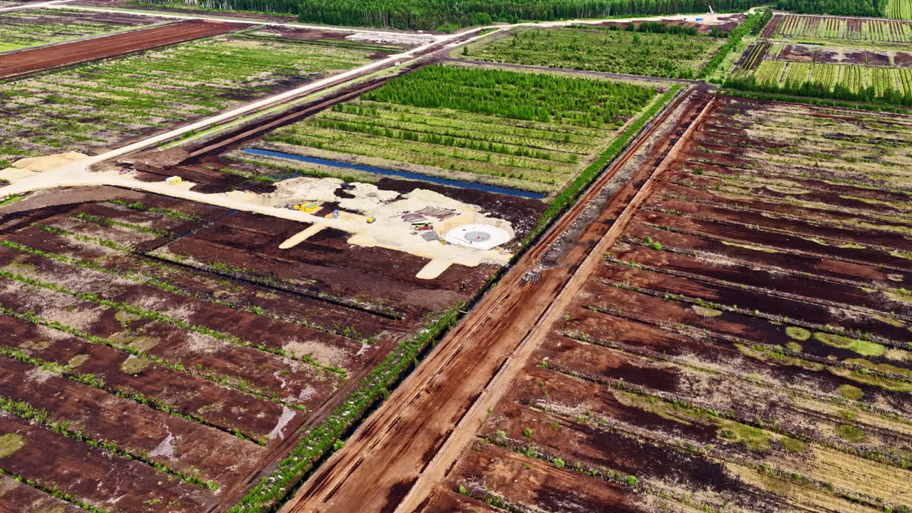 Wind turbine foundation construction site amid harvested peat fields in drone video