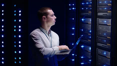 concept of digitalization of information: it specialist in front of server racks with laptop activates data center with a touch gesture. working on a laptop standing before open server rack cabinet