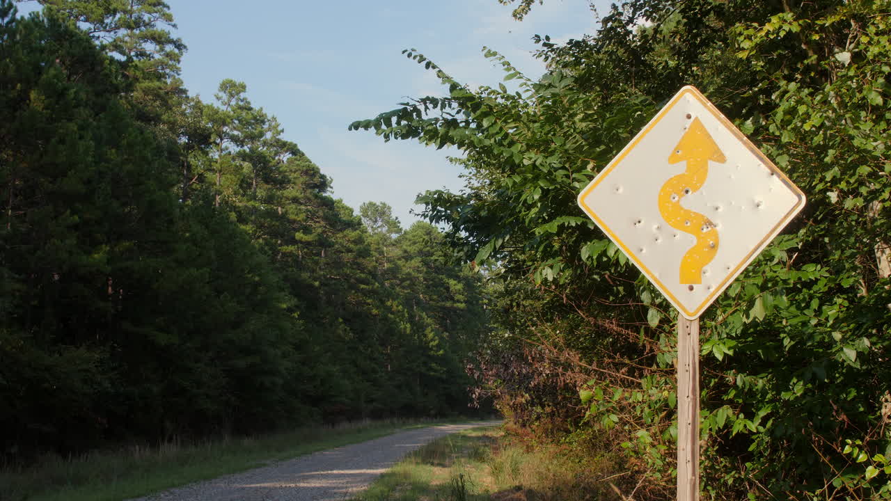 una toma amplia de una señal de advertencia de carretera que ha sido destrozada por múltiples disparos a lo largo de una carretera rural en el bosque nacional de ouachita, arkansas