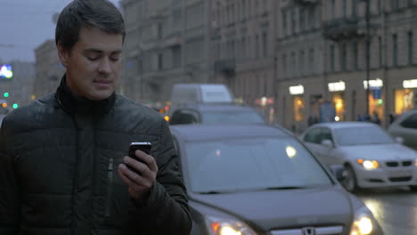 Hombre-Con-Teléfono-Celular-En-La-Ciudad-Lluviosa-De-Noche