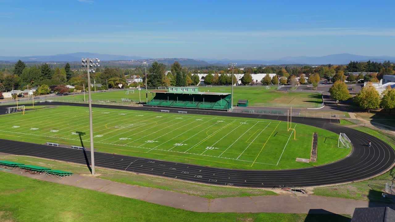 Wide aerial tracking shot of a lone woman on a high school running track
